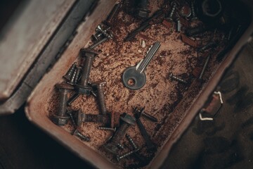 Top view of a silver key and rusty nuts and bolts in a box