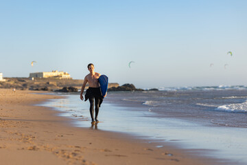 Fit man walking along the shore holding a surfboard