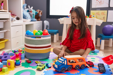 Adorable hispanic girl playing with car toy sitting on floor at kindergarten
