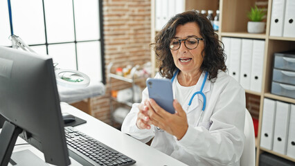 Middle age hispanic woman doctor doing video call with smartphone at the clinic