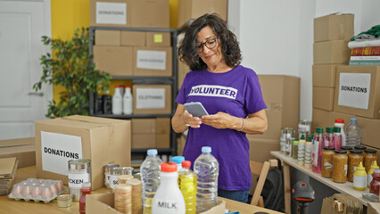 Middle age hispanic woman volunteer using smartphone checking products at charity center