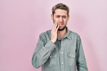 Hispanic man with beard standing over pink background touching mouth with hand with painful expression because of toothache or dental illness on teeth. dentist