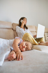 Fototapeta premium Baby sleeping near mother working remotely at home