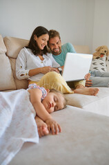 Mother and father using laptop near sleeping daughter