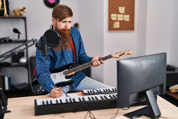 Young redhead man musician composing song playing electrical guitar at music studio