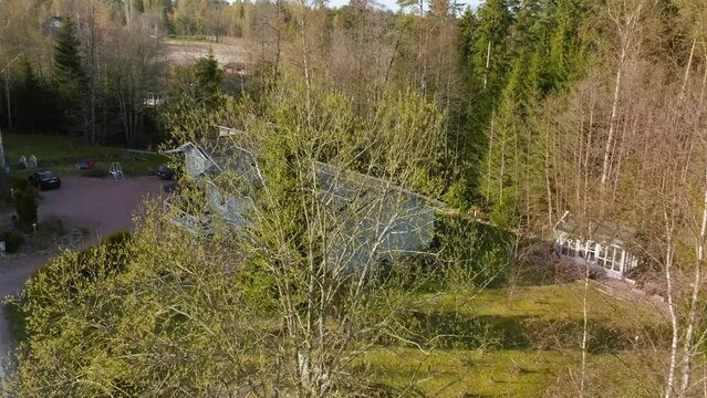 Aerial view of a rural house with solar panels surrounded by green trees on a sunny day