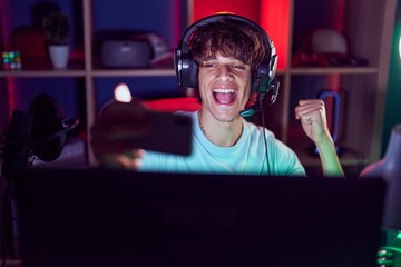 Hispanic young man playing video games with smartphone screaming proud, celebrating victory and...