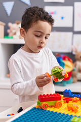 Adorable hispanic boy playing with construction blocks standing at kindergarten