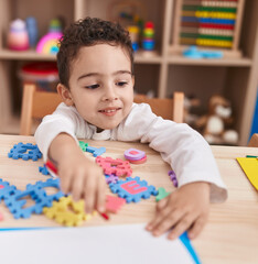 Adorable hispanic boy playing with vocabulary puzzle game sitting on table at kindergarten