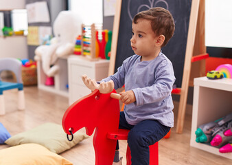 Adorable hispanic boy playing with reindeer rocking at kindergarten