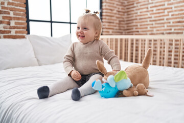Adorable blonde girl holding doll sitting on bed at bedroom