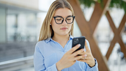 Young blonde woman business worker using smartphone with serious expression at street