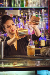 Smiling female bartender mixing burning cocktail at counter
