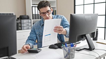 Young hispanic man business worker using computer reading document at office