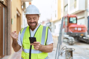 Middle age man architect using smartphone with winner expression at street