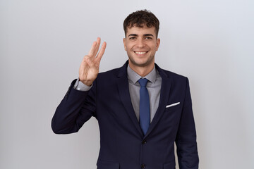 Young hispanic business man wearing suit and tie showing and pointing up with fingers number three while smiling confident and happy.