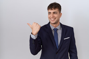 Young hispanic business man wearing suit and tie smiling with happy face looking and pointing to the side with thumb up.