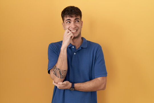 Young hispanic man standing over yellow background thinking worried about a question, concerned and nervous with hand on chin