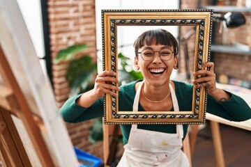 Young beautiful woman sitting at art studio with empty frame smiling and laughing hard out loud...