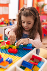 Adorable hispanic girl playing with construction blocks sitting on table at kindergarten