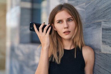 Fototapeta premium Young blonde woman listening to voice message with serious face at street