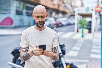Young bald man using smartphone with serious expression at street