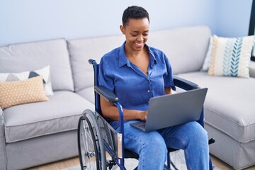African american woman using laptop sitting on wheelchair at home