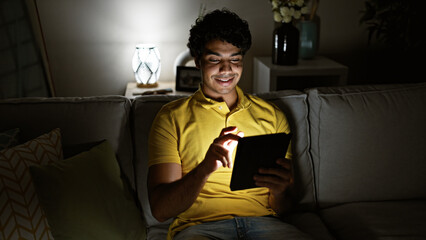 Young latin man using touchpad sitting on sofa at home