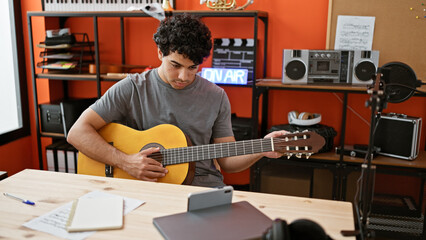 Young latin man musician having online classical guitar lesson at music studio