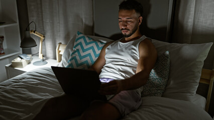 Young arab man using laptop sitting on the bed at bedroom