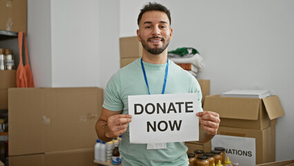 Young arab man volunteer holding donate now message smiling at charity center