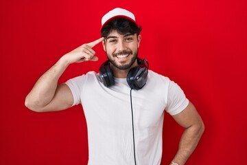 Hispanic man with beard wearing gamer hat and headphones smiling pointing to head with one finger, great idea or thought, good memory