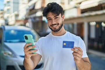 Young hispanic man using smartphone and credit card at street
