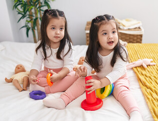 Adorable twin girls playing with hoops game sitting on bed at bedroom