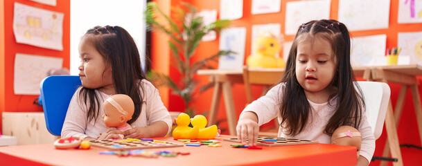 Adorable twin girls playing with maths puzzle game sitting on table at kindergarten