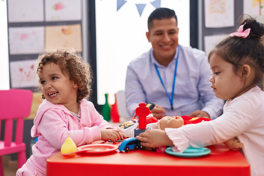 Hispanic man and girls playing supermarket game sitting on table at kindergarten