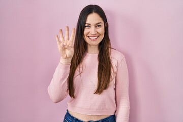 Young brunette woman standing over pink background showing and pointing up with fingers number four while smiling confident and happy.