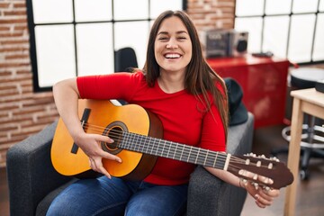 Young woman musician playing classical guitar at music studio