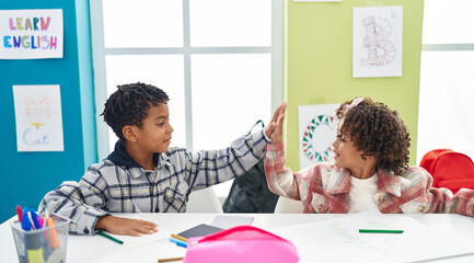 Adorable african american boy and girl students drawing on notebook high five at classroom