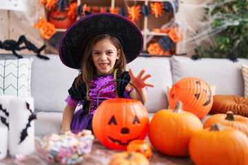 Adorable hispanic girl having halloween party doing scare gesture at home