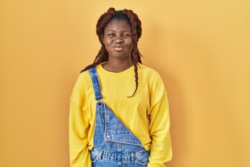 African woman standing over yellow background puffing cheeks with funny face. mouth inflated with air, crazy expression.