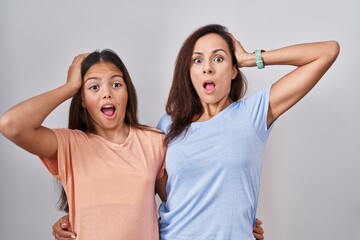 Young mother and daughter standing over white background crazy and scared with hands on head, afraid and surprised of shock with open mouth