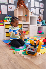 African american boy playing with car toy sitting on floor at kindergarten