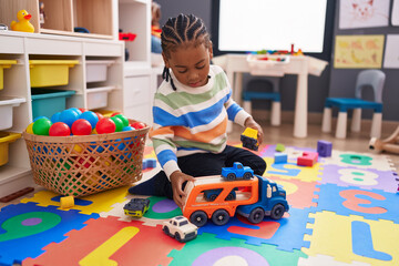 Fototapeta premium African american boy playing with car toy sitting on floor at kindergarten