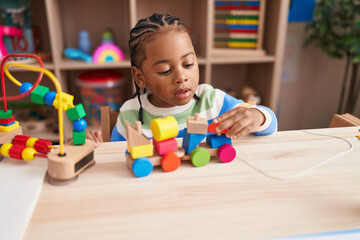 African american boy playing with blocks train toy sitting on table at kindergarten