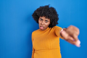 Fototapeta na wymiar Black woman with curly hair standing over blue background pointing displeased and frustrated to the camera, angry and furious with you