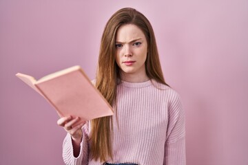 Young caucasian woman reading a book over pink background skeptic and nervous, frowning upset because of problem. negative person.