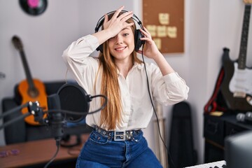 Young caucasian woman recording song at music studio stressed and frustrated with hand on head,...