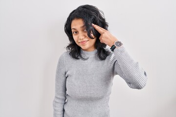 Hispanic woman with dark hair standing over isolated background shooting and killing oneself pointing hand and fingers to head like gun, suicide gesture.