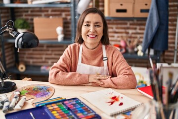 Fototapeta premium Middle age woman artist smiling confident sitting on table at art studio